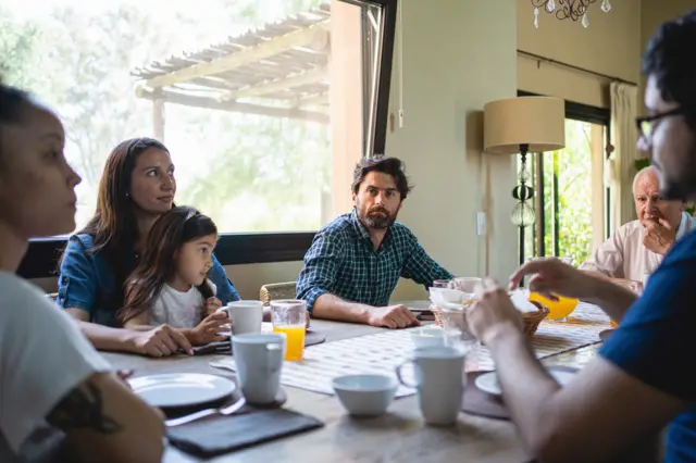 Una familia sentada en la mesa de la comida y uno de los hermanos observa a su hermana con recelo