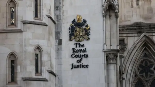 白いゴシック様式の建物にイギリスの国章が掲示され、その下に「The Royal Courts of Justice」と書かれている