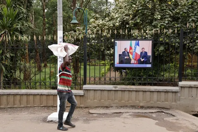 Un homme passe dans une rue devant une photo de Paul Biya et d'Emmanuel Macron dans une rue de Yaoundé