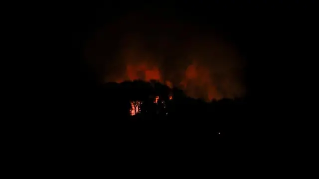 暗闇の中で建物の一部がオレンジ色に光り、オレンジ色の煙が上がっている