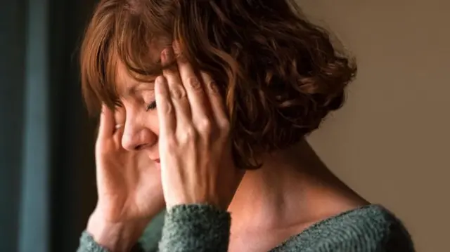 Una mujer de costado con las manos en sus sienes y los ojos cerrados