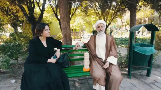صحنه‌ای از مستند عمامه صورتی که شخصیت آخوند فیلم با یک دختر روی نیمکتی در پارک صحبت می‌کند