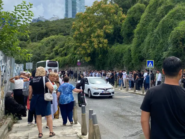 Birgün muhabiri Ebru Çelik'in paylaştığı fotoğrafta bir araba yolunun çevresinde bekleyen onlarca kişi görülüyor. Gazeteci Ebru Çelik bu kişilerin Kılıçdaroğlu'na destek için törene götürülen figüranlar olduğunu ileri sürüyor.