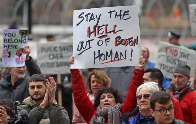 Una mujer en las protestas con un cartel que lee "Mantén el infierno lejos de Boston"