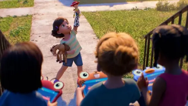 Niña en la entrada de una casa sosteniendo un muñeco vaquero en alto y otro juguete en la mano, mientras tres niños observan desde un porche con dispositivos electrónicos de colores.