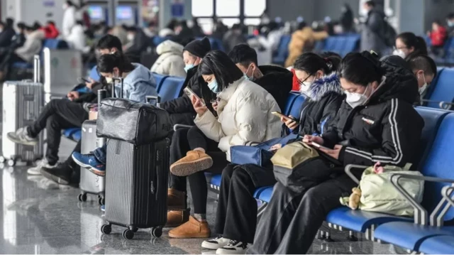 Hành khách đeo khẩu trang và xem điện thoại tại một ga tàu ở Trung Quốc