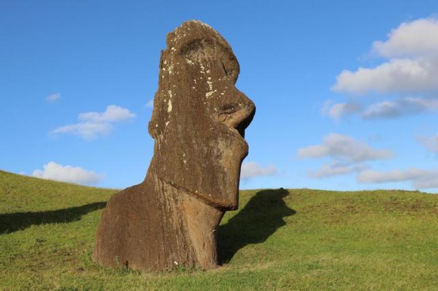 Estátua de uma cabeça gigante em um gramado sob um céu azul
