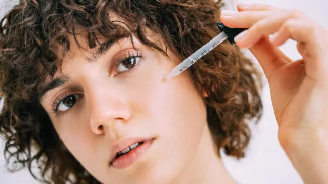 Una joven se aplica sérum en el rostro con una pipeta.