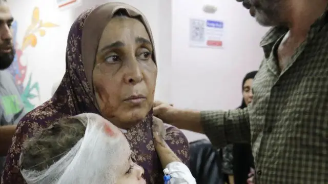 سيدة تحمل طفلاً مصاباً في مستشفى شهداء الأقصى بغزة