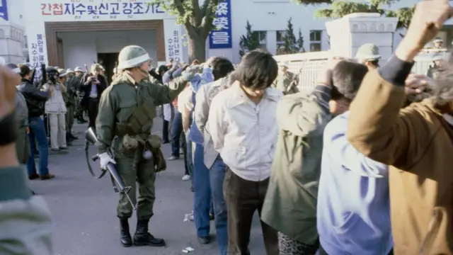 1980 年光州起义后，韩国武装部队突袭该市，逮捕了双手抱头的抗议者。