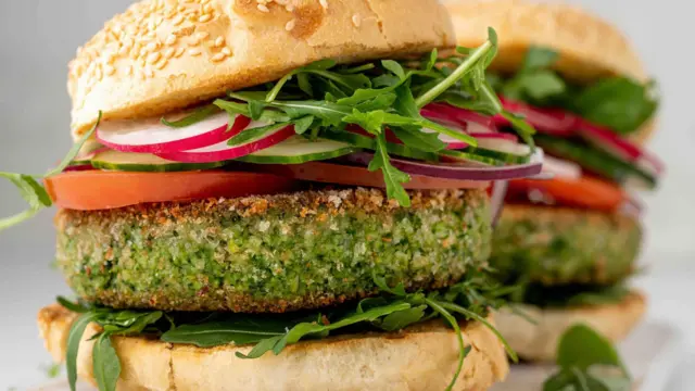 Zbliżenie na wegetariańskie burgery roślinne z rukolą i brokułami, plasterkami rzodkiewki, pomidorem i ogórkiem. Świeży wegański posiłek z menu wegetariańskiej restauracji. Bułka sezamowa na wierzchu bezmięsnej przekąski.