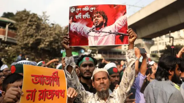 டாக்காவில் டிசம்பர் 19 அன்று ஷெரீஃப் உஸ்மான் ஹாதியின் மரணத்திற்குப் பிறகு நடந்த போராட்டத்தின் போது, போராட்டக்காரர் ஒருவர் அவரது புகைப்படத்தை ஏந்தியுள்ளார்.
