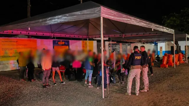 Imagem mostra cubanos com rostos embaçado embaixo de uma tenda, ao lado de agentes da PRF