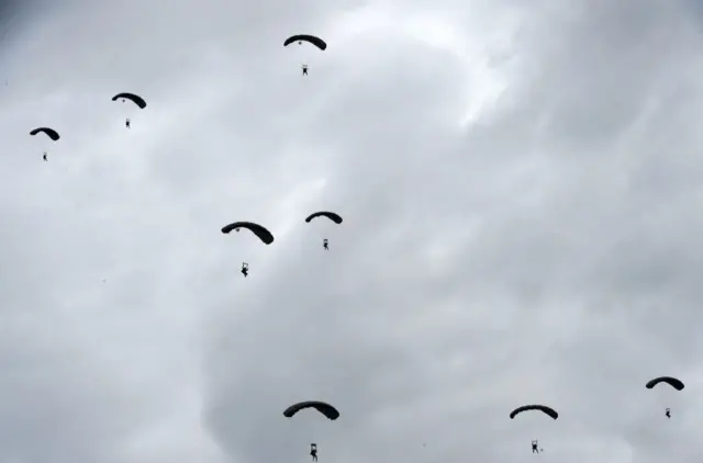 द्वितीय विश्वयुद्ध के दौरान 1944 में फ़्रांस के नॉरमैंडी में अमेरिकी सैनिकों के उतरने की वर्षगांठ पर जून 2022 में अमेरिकी पैराशूट सैनिक आसमान से पैराशूट से उतरते हुए.