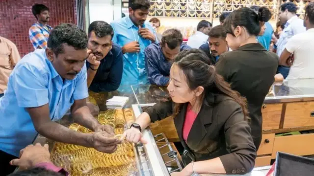 රත්ත්‍රන් භාණ්ඩ අලෙවිසැලක සිටින කාන්තාවකගෙන් යමක් ප්‍රශ්න කරන පුද්ගලයෙක්.