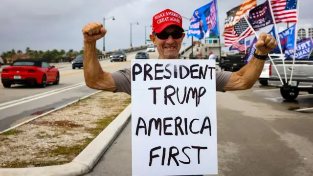 Um homem segura um cartaz que diz "Presidente Trump, Américadolphin pearls slotprimeiro lugar".