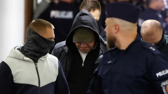 Володимир Журавльов у капюшоні, з опущеним обличчям заходить до зали суду у супроводі двох співробітників польської поліції 