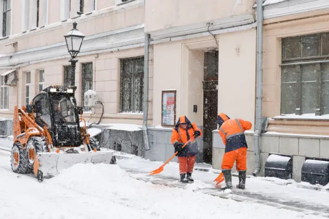 Снегоуборочная машина и дворники убирают снег на одной из улиц в центре Москвы