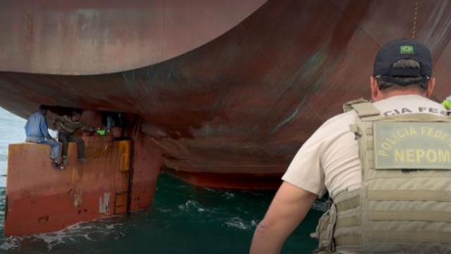 policial em barco olhando imigrantes no leme do navio