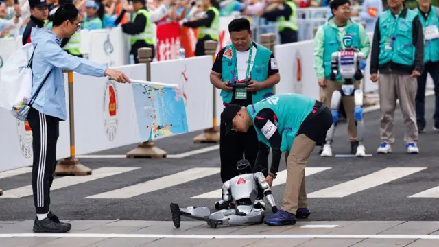 ربات به زمین افتاده و مربیاش در حال کمک به او برای بلند شدن است