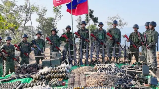 အေအေသတင်းထုတ်ပြန်ရေးအဖွဲ့က ထုတ်ပြန်တဲ့ ဓာတ်ပုံဟောင်း တစ်ပုံဖြစ်ပါတယ်။ တူညီဝတ်စုံ ယူနီဖောင်း၊ ဦးထုပ်ဆောင်းပြီး ရိုင်ဖယ်သေနတ်တွေကို အောက်စိုက်ကိုင်ထားတဲ့ အမျိုးသား ၁၀ ဦးထက်မနည်းကို သူ့တို့ရဲ့ရှေ့မှာ ကျည်ဆန်တွေ၊ မိုင်းတွေ စုပြုံ ခင်းကျင်းထားတဲ့ ဓာတ်ပုံဖြစ်ပါတယ်။ ဓာတ်ပုံအလယ်မှာ အနီအပြာစပ် အေအေနဲ့ ရခိုင်အလံ နှစ်ခု လွှင့်ထူထားတာကို တစိတ်တစ်ပိုင်းမြင်တွေ့ရ၊ အနောက်ဘက်မှာ သစ်ပင်အချို့နဲ့ တောင်တန်းပြပြကို မြင်ရ 
