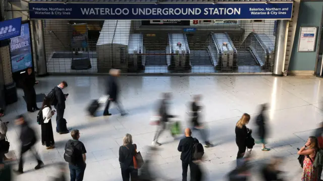 Вход в лондонское метро закрыт решеткой, около него видны размытые силуэты проходящих мимо людей