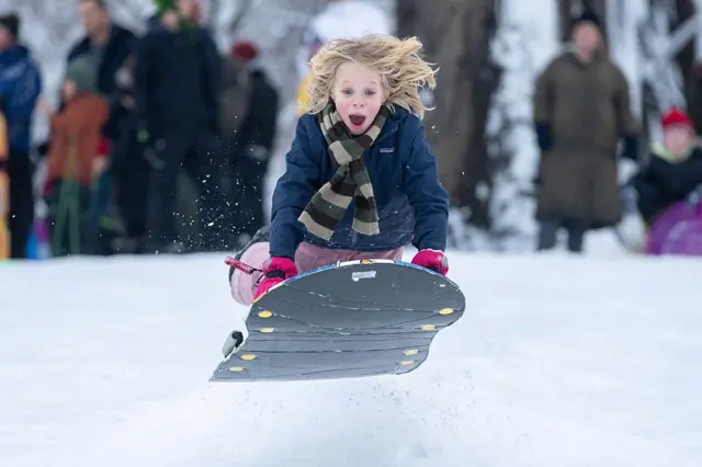 Kızağıyla bir kar birikintisinden havaya sıçrayan bir çocuk