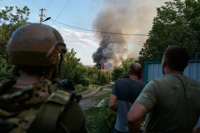 Ukraińscy żołnierze i mieszkańcy obserwują płonące domy podczas rosyjskiego nalotu 14 sierpnia 2025 r. w Słowiańsku na Ukrainie. 