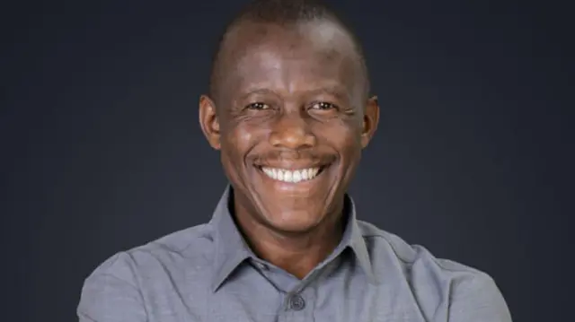 Humphrey Polepole ariko aramwenyura. Yambaye ishati isa n'igipfungu