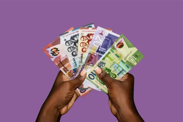Main tenant plusieurs billets de cedi ghanéens.