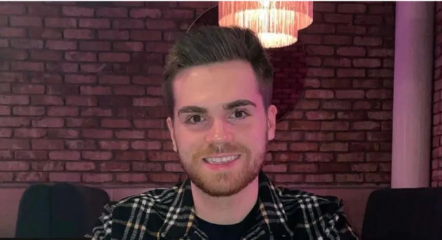 Hugh kameraya bakıyor ve gülerek poz veriyor.