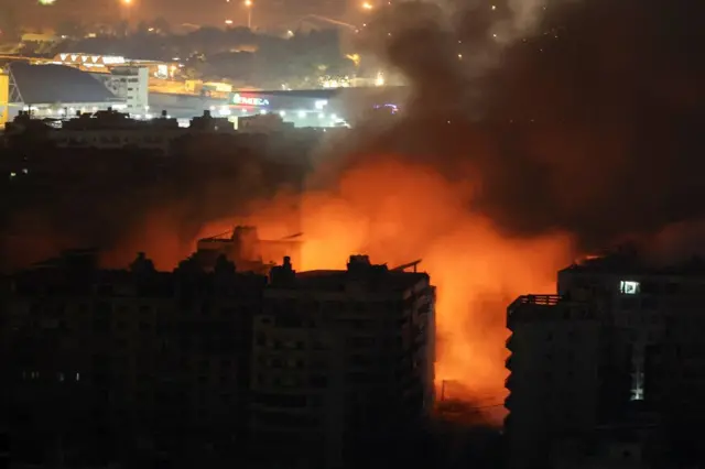 Fogo e fumaça em meio a prédios durante a noite