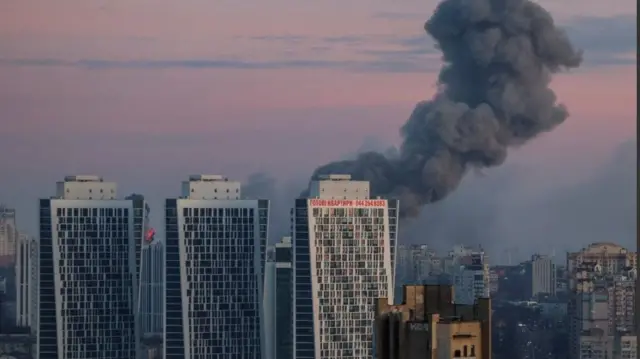 Три висотки вранці над Києвом, позаду рожево-голубе небо і величезний стовп диму, грудень 2023 року