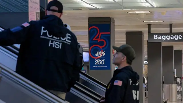 Dois policiais subindo uma escada rolante em um aeroporto aparentemente vazio