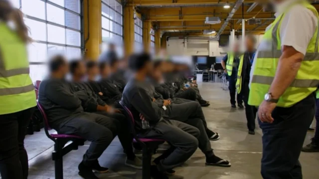 নিরাপত্তারক্ষীদের সামনে বসে আছেন এক ডজনেরও বেশি মানুষ যাদের পরিচয় গোপন রাখতে ছবিতে চেহারা ঘোলা করে রাখা হয়েছে