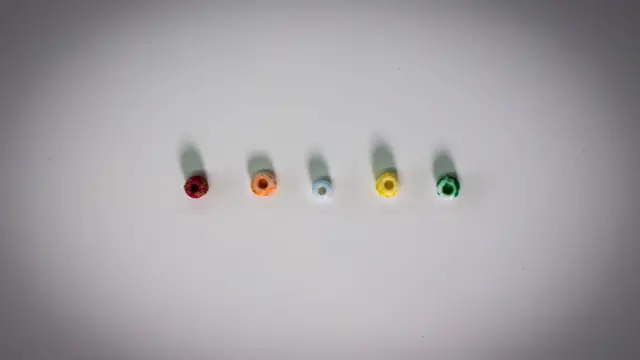 Пʼять маленьких намистин на білому тлі: червона, помаранчева, блакитна, жовта, зелена