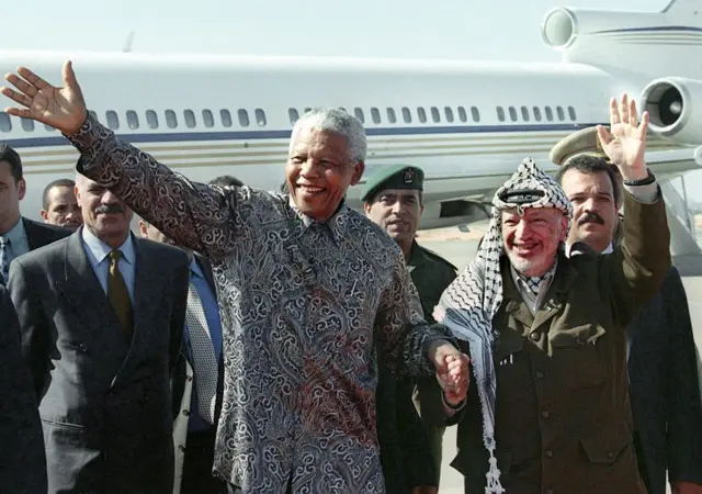 Yasser Arafat et l'ancien président sud-africain Nelson Mandela saluent la foule lors de leur rencontre à l'aéroport international de Gaza, à Rafah, le 19 octobre 1999