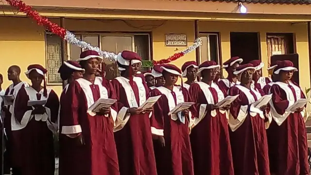 Aworan awọn ẹgbẹ akọrin ti wọn wọ aṣọ pupa, wọn de fila wọn si mu iwe orin dani