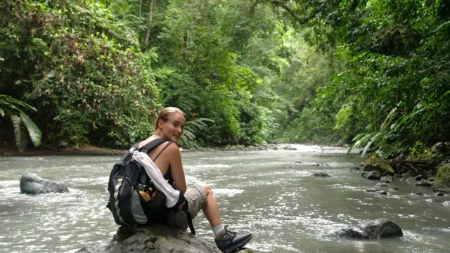Una excursionistra con una mochila a cuestas descansa en una roca de un río en el Parque Nacional Corcovado