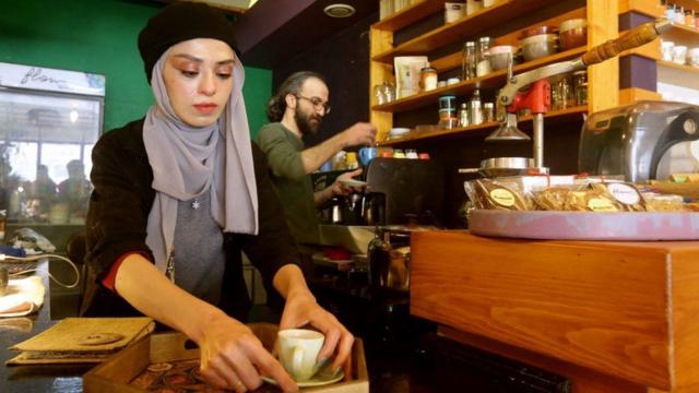 Una mujer sirve un café en una cafetería en Damasco