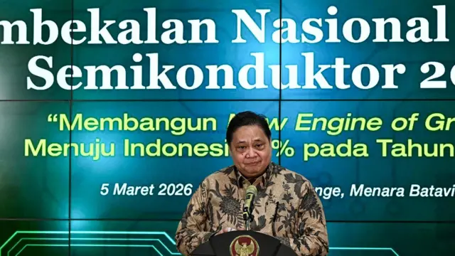 Menko Bidang Perekonomian Airlangga Hartarto menggunakan baju batik berada di atas podium dengan latar belakang layar proyeksi LCD.