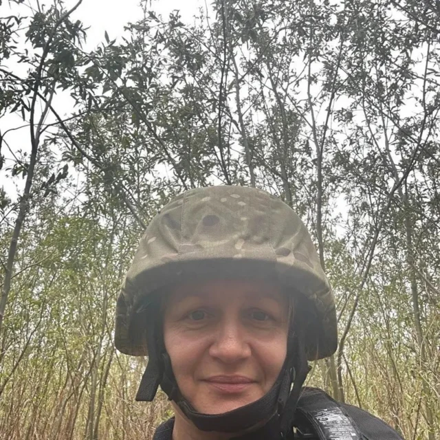 Женщина в каске на фоне молодых деревьев или высоких кустов