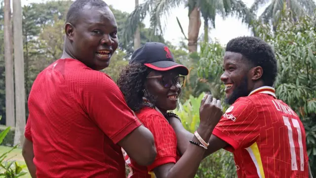 Three Liverpool fans in Uganda larking about in front of the camera in a garden in Kampala