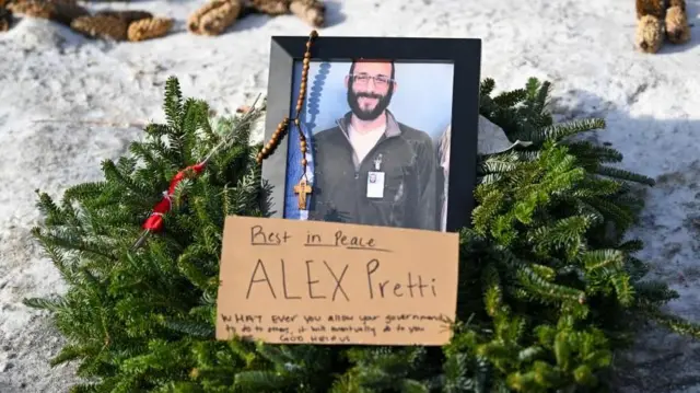 プレティさんの笑顔の写真が黒いフレームに入れられ、常緑樹の葉のリースや木製のロザリオと共に、雪の上に供えられている