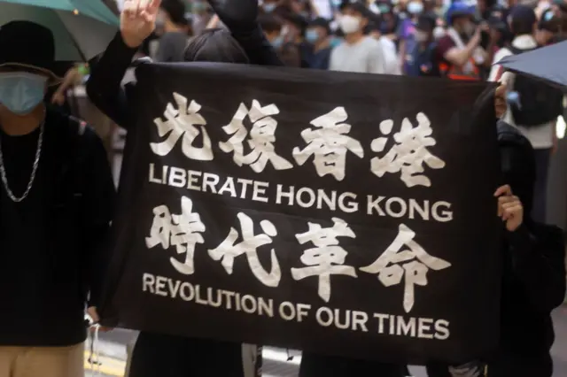 Bango jeusi linasomeka "ikomboe Hong Kong - Mapinduzi ya Nyakati Zetu" kwa Kiingereza na Kichina