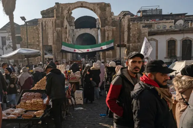 Yeni Suriye bayrağı, palmiye ağaçları, kalabalık bir pazar yeri