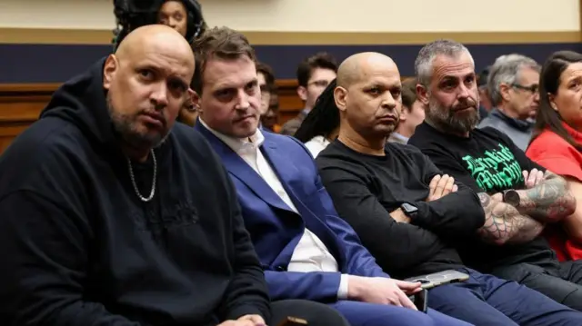 司法委公聴会の傍聴席に、4人の男性が厳しい表情で並んで座っている。うち2人は腕を組んでいる