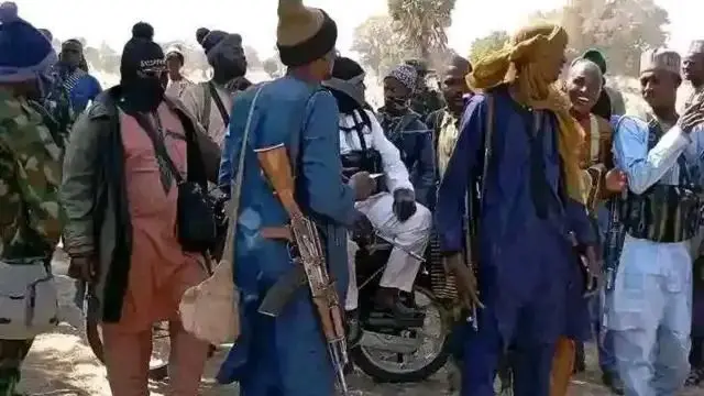 Wasu ƴanfashin daji riƙe da bindigogi a tare wani mai farin tufafi zaune a kan babur