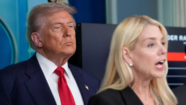 Trump ao fundo enquanto Pam Bonid, uma mulher loira discursa. 