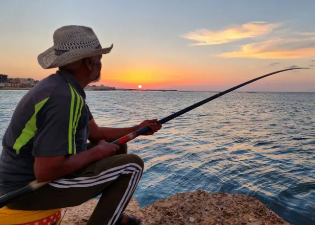 The sun sets over the Mediterranean Sea in Libya, where a fisherman bides his time on Tripoli's waterfront on Monday.